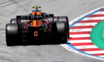 Orange Formula 1 car speeding around a track curving onto red-and-white striped curb and blue paint edge (Etihad sponsor on rear wing).
