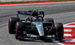Mercedes-AMG Petronas Formula 1 car navigating a red-and-white curbed corner on a racetrack, driver in helmet visible behind the cockpit.