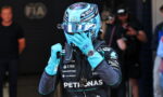 F1 driver in blue Petronas helmet and suit adjusting his glove in the pit area with team branding visible