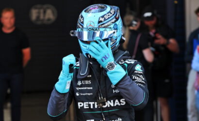 F1 driver in blue Petronas helmet and suit adjusting his glove in the pit area with team branding visible