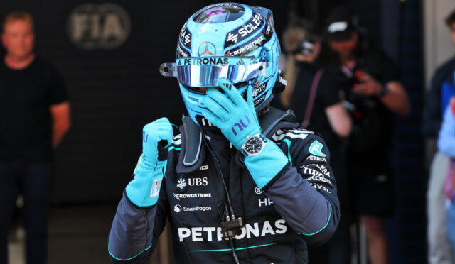 F1 driver in blue Petronas helmet and suit adjusting his glove in the pit area with team branding visible
