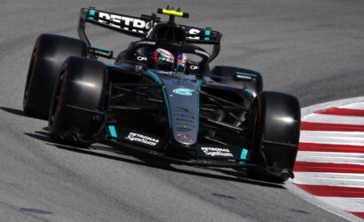 Mercedes‑AMG Petronas Formula 1 car taking a tight corner on a race track, front wing close to the red‑and‑white curbs, sponsor logos visible