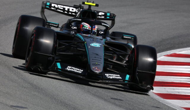 Mercedes‑AMG Petronas Formula 1 car taking a tight corner on a race track, front wing close to the red‑and‑white curbs, sponsor logos visible