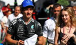 Young race car driver in a black Mercedes team shirt and blue cap, surrounded by fans at an event, with a woman beside him.