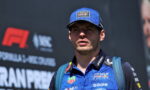 Male race car driver in a blue Oracle Red Bull Racing shirt and cap, speaking at a track with sponsor logos visible on the jersey and background.