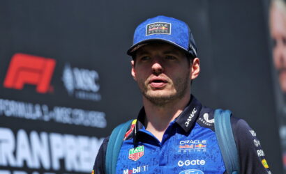 Male race car driver in a blue Oracle Red Bull Racing shirt and cap, speaking at a track with sponsor logos visible on the jersey and background.