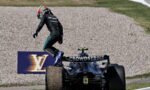 Formula 1 driver in a black Petronas suit jumps from a CrowdStrike–branded F1 car onto the gravel runoff at the track edge.