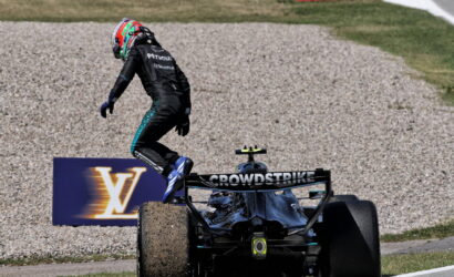 Formula 1 driver in a black Petronas suit jumps from a CrowdStrike–branded F1 car onto the gravel runoff at the track edge.