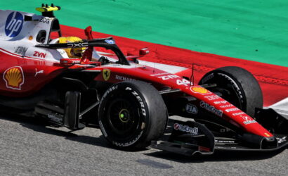 Red Ferrari Formula 1 car on a race track, front wing close to the ground, sponsorship logos visible on the chassis and tires.