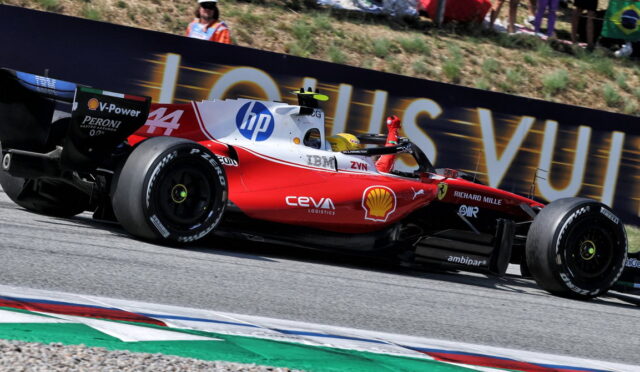Red Ferrari Formula 1 car speeding along a track with sponsor logos (Shell, HP) and a Louis Vuitton banner in the background, spectators nearby.
