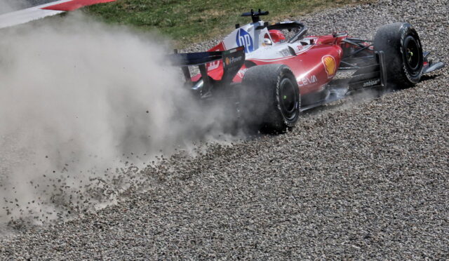 Red Formula 1 car skidding on a gravel runoff while kicking up a cloud of dust and rocks.