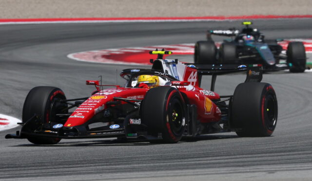 Red Ferrari Formula 1 car leads a tight midfield pack around a sweeping race corner on the track, sponsor logos visible on bodywork