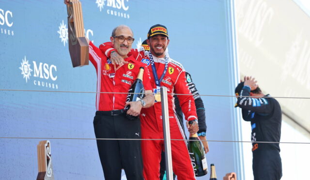 Two Ferrari drivers celebrate on the podium, one raises a wooden trophy while the other holds a champagne bottle and wears a medal, against a blue MSC Cruises backdrop.