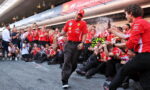 Red-clad Ferrari team celebrations: a man walks forward as teammates spray champagne in a pit lane.