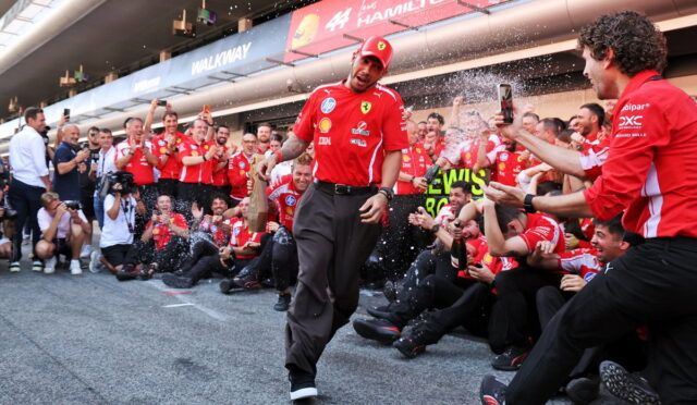 Red-clad Ferrari team celebrations: a man walks forward as teammates spray champagne in a pit lane.
