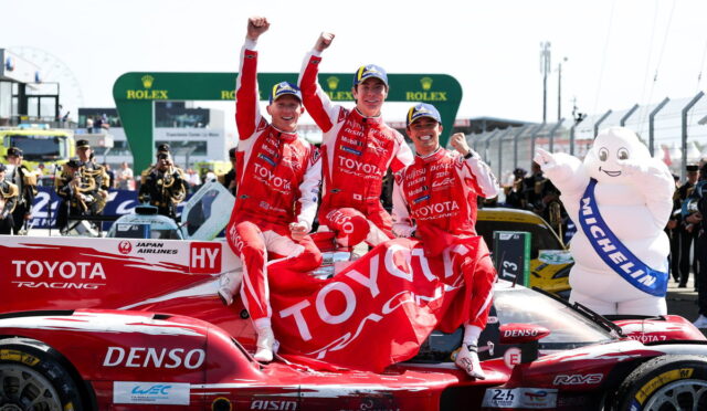 Three Toyota Racing drivers celebrate on a red race car, raising their fists with a large Toyota banner in the background.]"