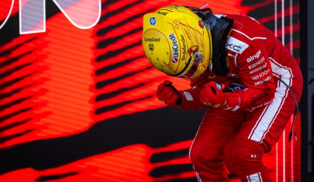 F1 driver in a red racing suit and yellow helmet leans forward in a victory celebration against a red LED backdrop simple, bold colors.