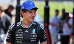Young man in a black Mercedes racing jersey and a blue cap with the Mercedes star, standing outdoors at a event.
