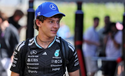 Young man in a black Mercedes racing jersey and a blue cap with the Mercedes star, standing outdoors at a event.