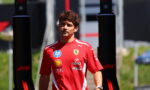 Ferrari team member in a red shirt with sponsor logos standing outdoors between black pit structures.