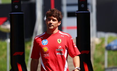 Ferrari team member in a red shirt with sponsor logos standing outdoors between black pit structures.