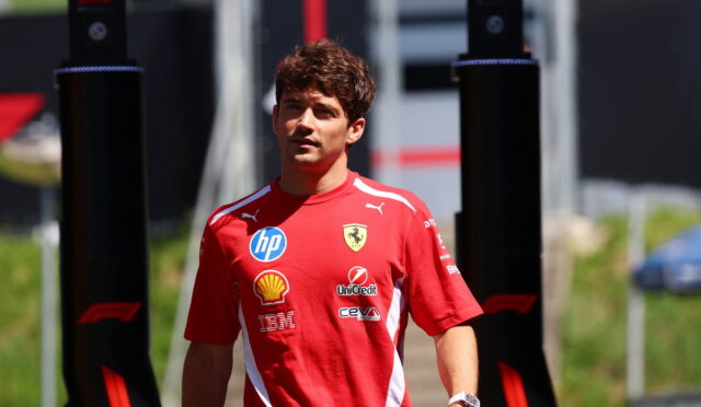 Ferrari team member in a red shirt with sponsor logos standing outdoors between black pit structures.