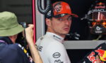 Race car driver in a white sponsor suit looks over his shoulder in a garage, photographer on the left taking a photo.