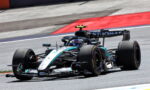 Formula 1 car from Mercedes on a race track, cornering at speed with red and blue curbs in the background.