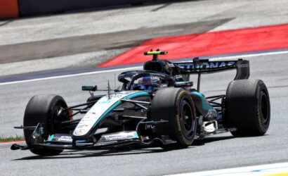 Formula 1 car from Mercedes on a race track, cornering at speed with red and blue curbs in the background.