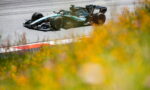 Formula 1 car from the Mercedes Petronas team speeding through a corner on the track, with yellow flowers blurred in the foreground.