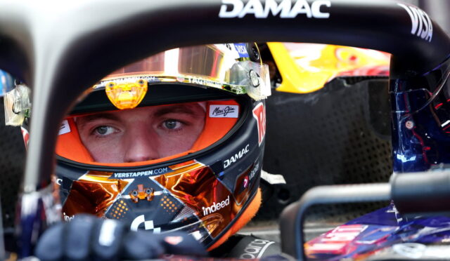 Close-up of a race car driver in a colorful helmet seated in a Formula 1 cockpit, DAMAC branding visible on the halo bar.