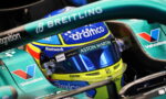 Close-up of a Formula 1 driver's helmet inside a teal Aston Martin car, featuring Aramco, Valvoline, and Breitling logos act as sponsors.