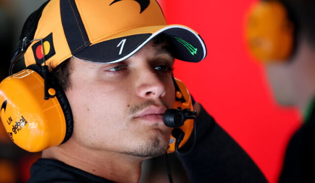 Man wearing a yellow racing headset and cap, focused in a pit area with a red background behind him.