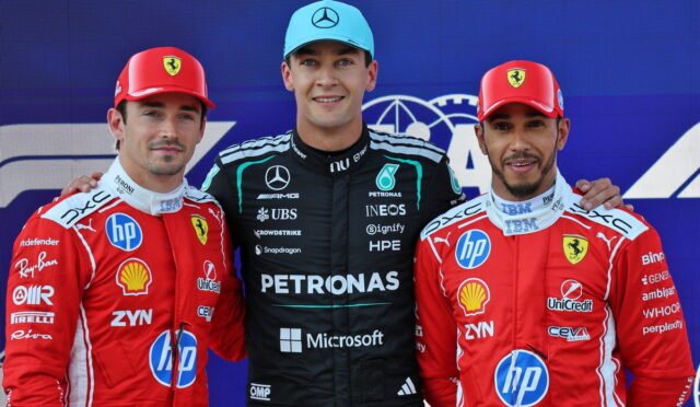 Three Formula 1 drivers pose on a podium; center driver in black Petronas suit and blue cap, flanked by Ferrari drivers in red suits with hands on shoulders.