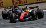 Two Formula 1 cars race side by side on a track, with yellow Pirelli barriers in the background.