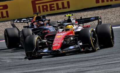 Two Formula 1 cars race side by side on a track, with yellow Pirelli barriers in the background.