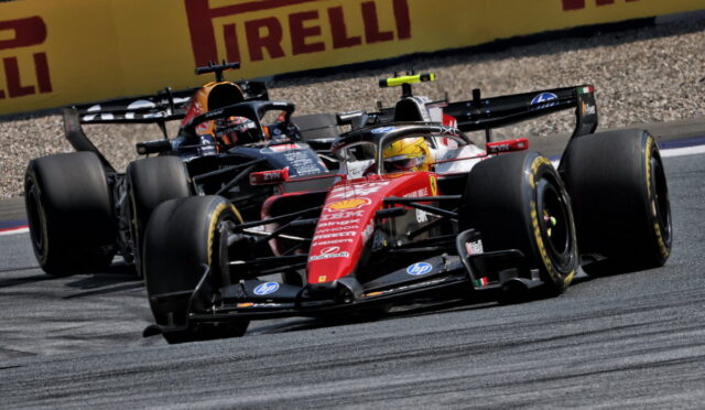 Two Formula 1 cars race side by side on a track, with yellow Pirelli barriers in the background.