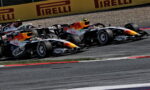 Two Red Bull Formula 1 cars race side by side on a track, leaning into a corner with Pirelli banners in the background.