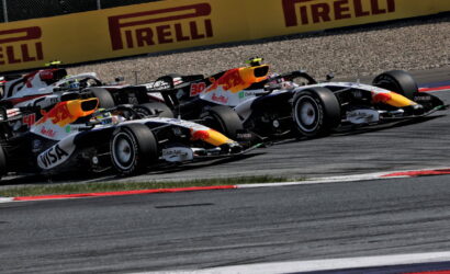 Two Red Bull Formula 1 cars race side by side on a track, leaning into a corner with Pirelli banners in the background.