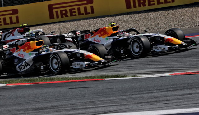 Two Red Bull Formula 1 cars race side by side on a track, leaning into a corner with Pirelli banners in the background.