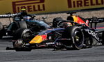 Two Formula 1 cars race side by side on a track, with a Red Bull Oracle-sponsored car in the foreground and a teal Mercedes behind, Pirelli ads in the background.