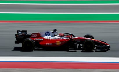 Red Formula 1 race car speeding along a track with sponsor logos (HP, Shell, Ferrari) and motion blur in the background.