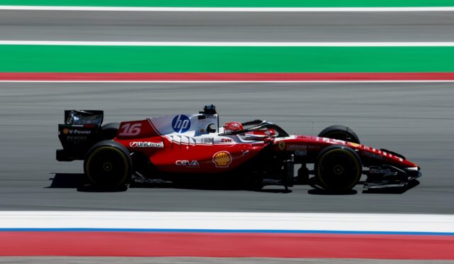 Red Formula 1 race car speeding along a track with sponsor logos (HP, Shell, Ferrari) and motion blur in the background.