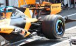 Close-up of an orange McLaren Formula 1 car in the garage, showing the rear wing with sponsor logos (Dropbox) and a Pirelli tire in the foreground.