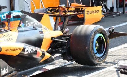Close-up of an orange McLaren Formula 1 car in the garage, showing the rear wing with sponsor logos (Dropbox) and a Pirelli tire in the foreground.