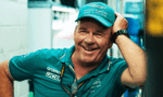 Smiling man in teal Aston Martin Formula One Team cap and polo, leaning with hand on his head.