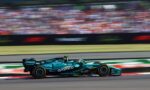 Teal Formula 1 car racing at full speed on a track, with a blurred grandstand in the background.