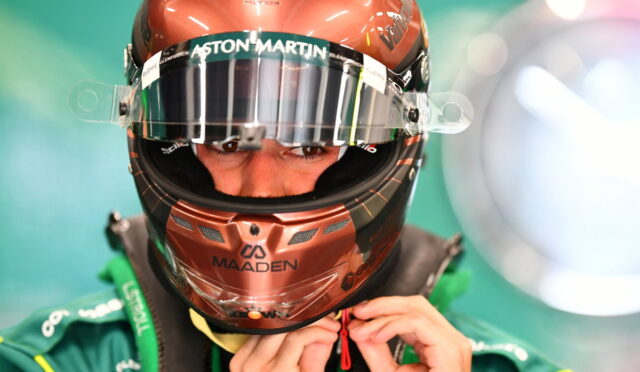 Close-up of a race car driver in a bronze helmet with Aston Martin branding, tightening the visor strap.