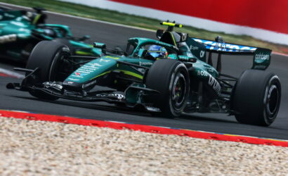Green Formula 1 race car corners at high speed on a race track with gravel trap and red barriers nearby.