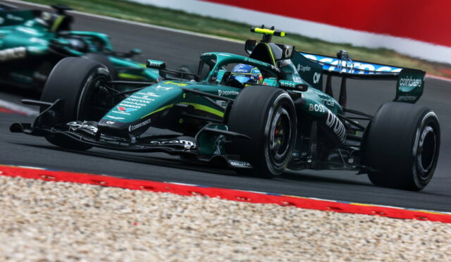 Green Formula 1 race car corners at high speed on a race track with gravel trap and red barriers nearby.
